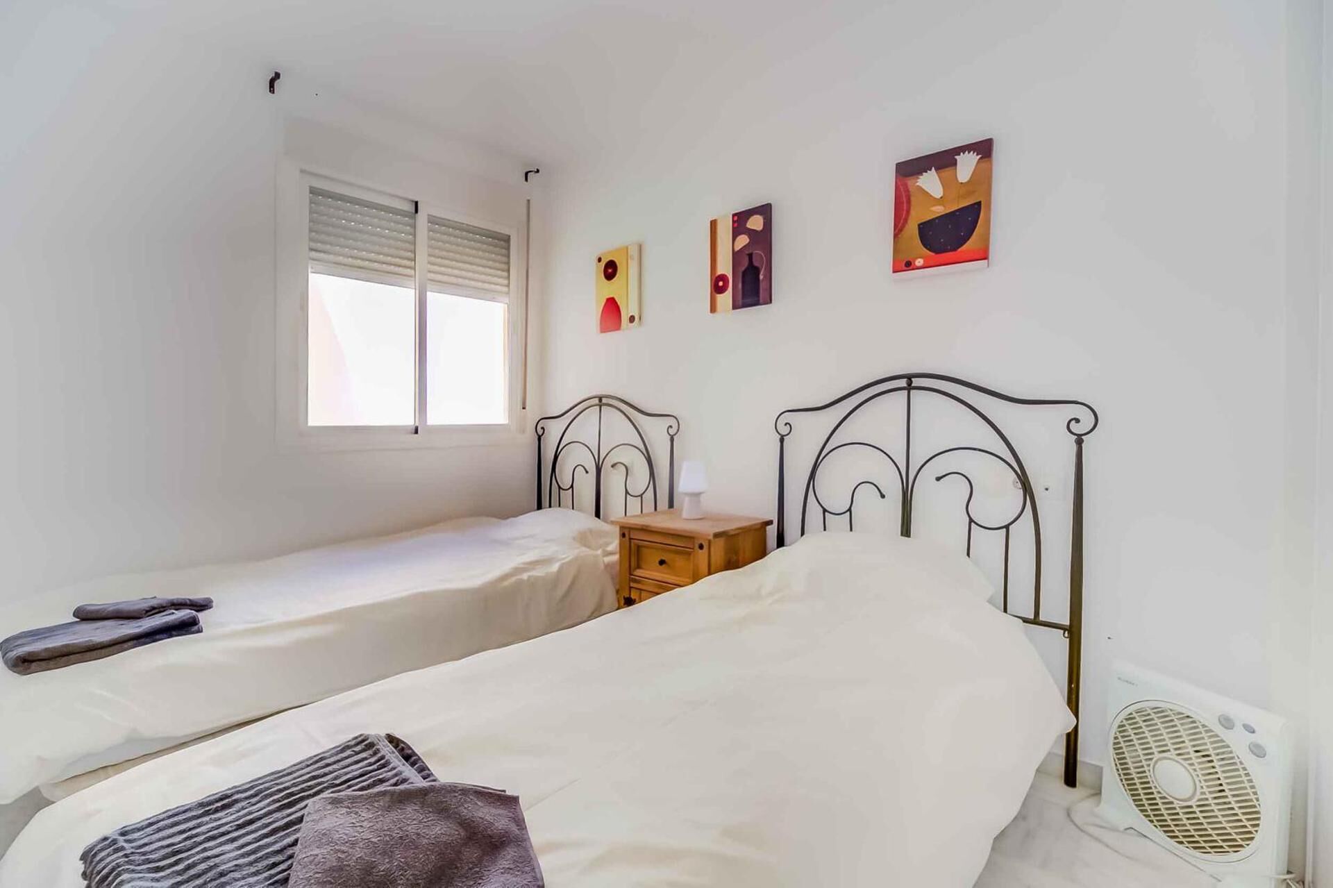 Una camera da letto con due letti singoli, una finestra con persiane, un comodino con lampada e un termosifone a parete.