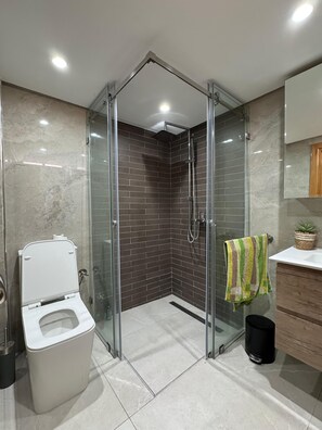 A modern bathroom with a glass-enclosed shower, a toilet, and a sink with a wooden cabinet.