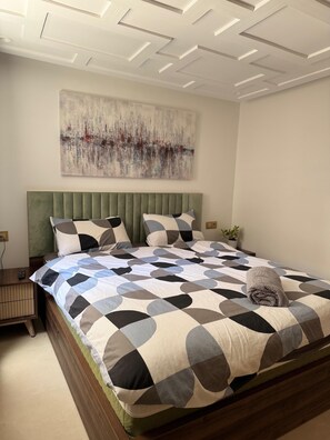A bedroom with a bed, a nightstand, a wall-mounted abstract painting, and a ceiling with recessed lighting.