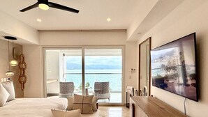 Ett modernt hotellrum med en stor säng, en TV, en balkong med stolar och utsikt över havet.
