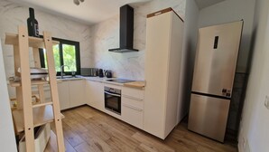 Una cocina moderna con armarios blancos, horno integrado, refrigerador de acero inoxidable y una escalera de madera.