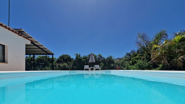 Una piscina azul cristalina con sillones de descanso y una pérgola al fondo.