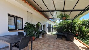 Un patio al aire libre con una zona de estar cubierta, una mesa de comedor y plantas en macetas.