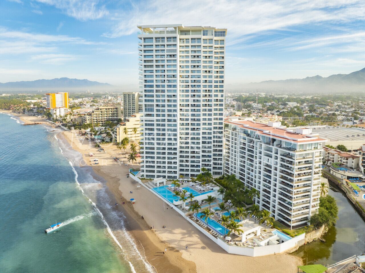 Un hotel moderno de gran altura con varios balcones, ubicación frente a la playa y zona de piscina.