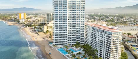 A high-rise hotel with multiple balconies, a beachside location, and a pool area.