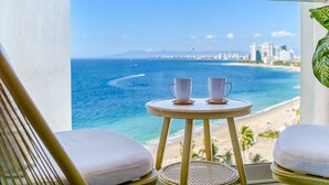 Ein Balkon mit Meerblick, zwei weiße Stühle und ein runder Tisch mit zwei weißen Tassen.