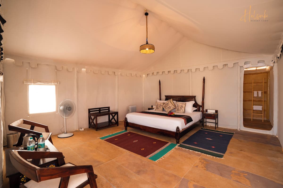 A bedroom with a bed, bedside tables, a desk, a chair, a fan, and a window.