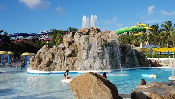 Ein Wasserpark mit einer großen Felsformation, einer Wasserrutsche und einem Poolbereich.