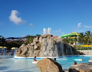A water park with a large rock formation, a water slide, and a pool area.