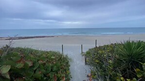 Ein Weg, der zu einem Strand mit Blick auf das Meer und einen bedeckten Himmel führt.