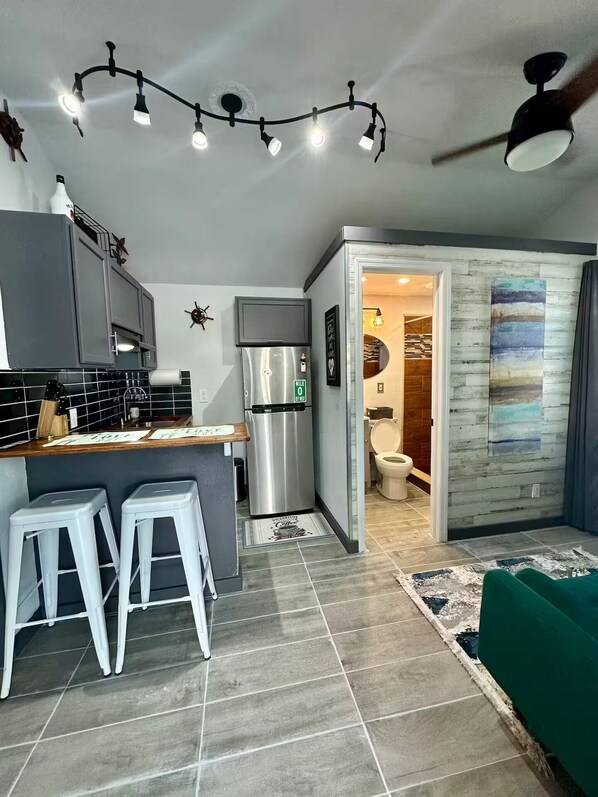 A modern kitchen with grey cabinets, a stainless steel refrigerator, and a bar area with stools.
