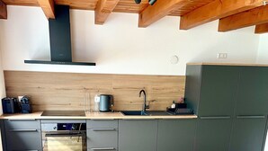 Une cuisine moderne avec des poutres en bois au plafond, un four encastré et un plan de travail noir.