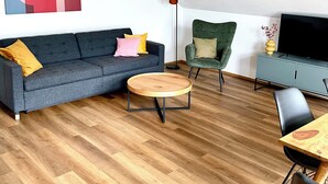 Un salon moderne avec un canapé gris, une table basse ronde en bois, un fauteuil vert et une table à manger avec des chaises.