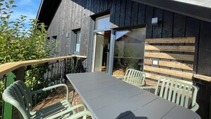 Un espace de restauration en plein air avec une table et des chaises, une terrasse en bois et un bâtiment à la façade sombre et aux grandes fenêtres.