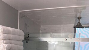 Una ducha con cerramiento de vidrio, cabezal de ducha de mano y llave de pared.