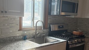 Una cocina con armarios blancos, una estufa de acero inoxidable, un microondas y una ventana con vistas al exterior.