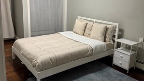 Un dormitorio con cama, mesita de noche, ventana con cortinas y una lámpara en el techo.