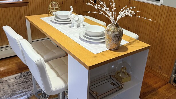 Un comedor con una mesa de madera, sillas blancas y un jarrón decorativo.
