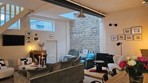 A spacious living room with a stone wall, a staircase, and a large window. - Spacious family house Elegant 6 pers. 3 *|Center and Quiet - Ste Catherine (Honfleur)