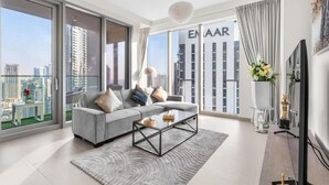 A modern living room with a grey sofa, a glass coffee table, and a large window with a city view. - Roomszy Forte Residences Downtown Dubai (Dubai)