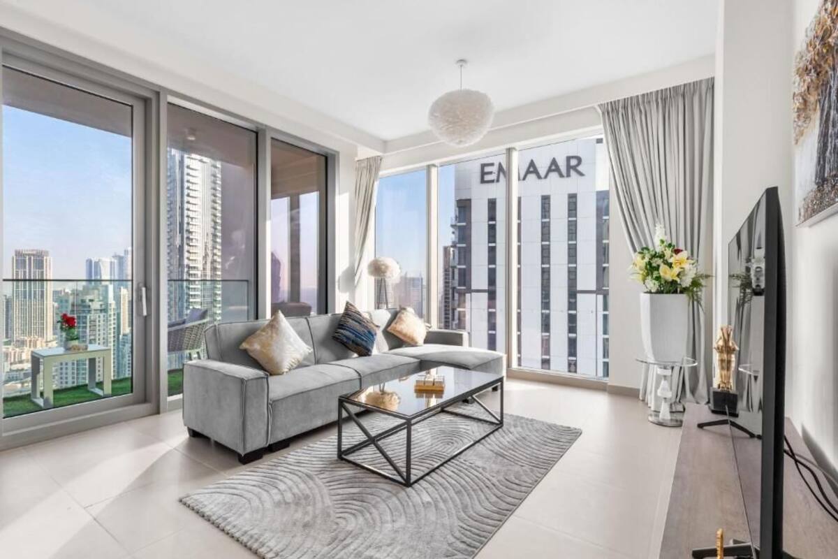 A modern living room with a grey sofa, a glass coffee table, and a large window with a city view.
