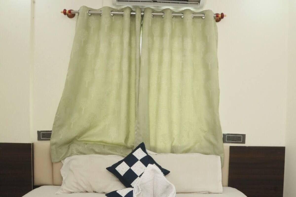 A neatly made bed with a folded towel and a blanket, a checkered pillow, and a green curtain.