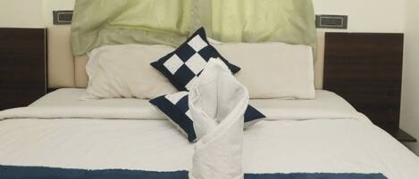 A neatly made bed with a folded towel and a blanket, a checkered pillow, and a green curtain.