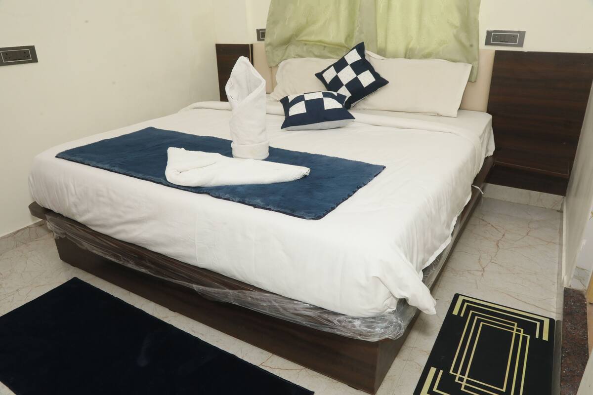 A neatly made bed with a blue blanket, white pillows, and a folded towel.