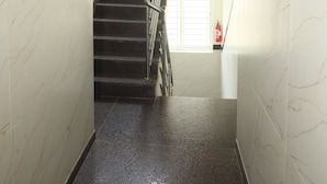A stairwell with marble walls and a metal railing, leading to a landing with a window and a fire extinguisher. - Hotel Rest O ITPL (Bangalore)