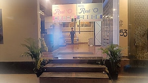 A hotel entrance with a reception desk, a sign indicating 24/7 A/C room service, and a number 53 on the wall. - Hotel Rest O ITPL (Bangalore)