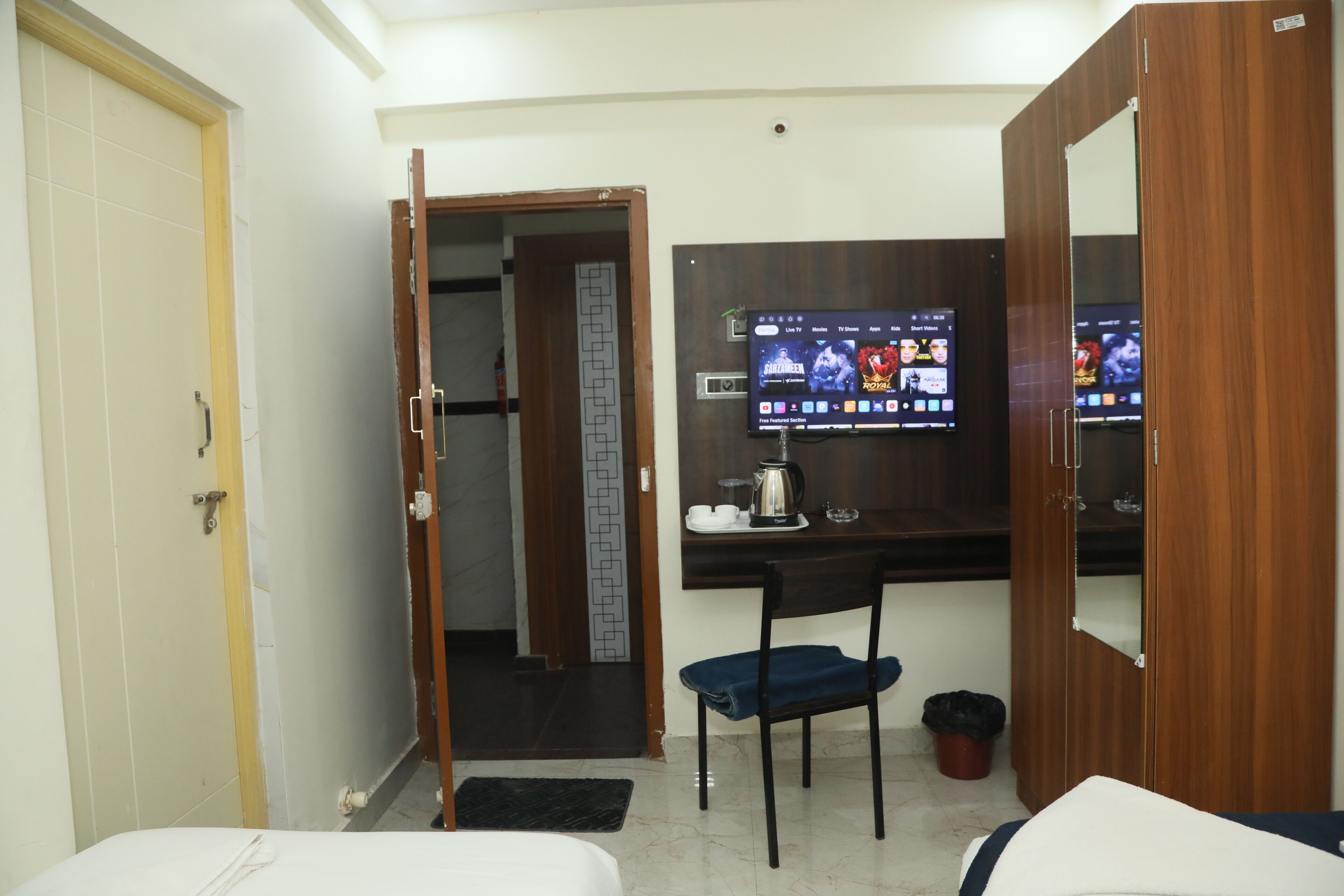 A hotel room with a bed, a desk with a computer monitor displaying various apps, a chair, and a wardrobe.