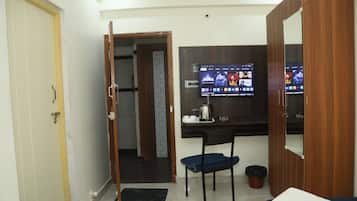 A hotel room with a bed, a desk with a computer monitor displaying various apps, a chair, and a wardrobe.