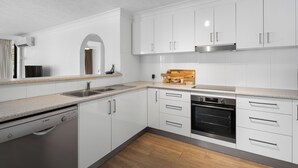 A modern kitchen with white cabinetry, a Bosch dishwasher, a built-in oven, and a wooden countertop. - Stylish 3BRM Haven in Surfers Paradise (Surfers Paradise)