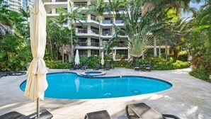 A swimming pool with lounge chairs and umbrellas, surrounded by palm trees and a multi-story building. - Stylish 3BRM Haven in Surfers Paradise (Surfers Paradise)