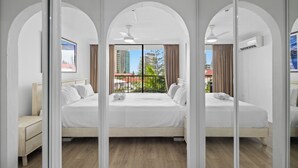 A modern hotel room with two beds, a wooden floor, and a balcony with a view of buildings and greenery. - Stylish 3BRM Haven in Surfers Paradise (Surfers Paradise)