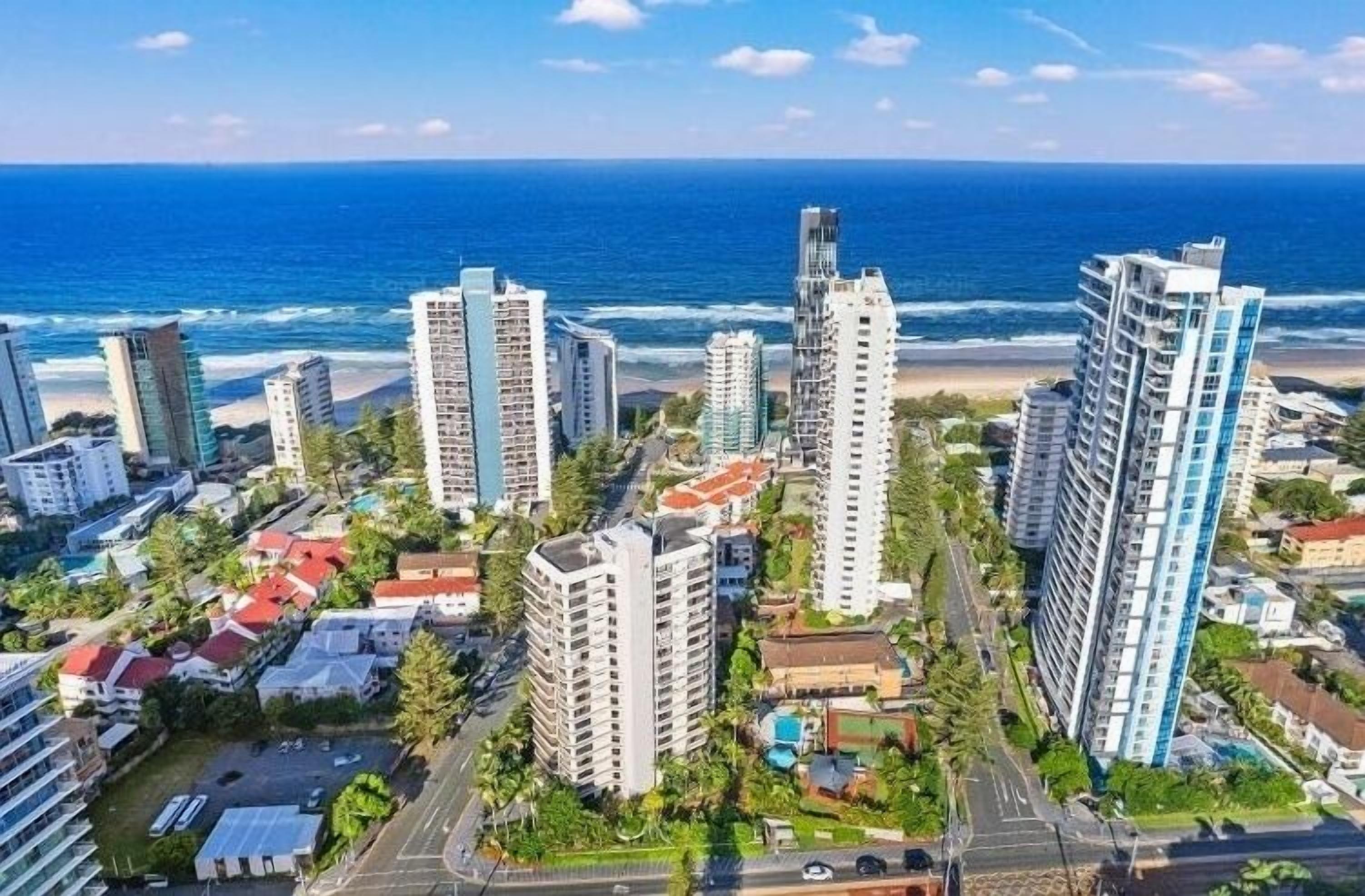 A coastal cityscape with high-rise buildings, a beach, and a clear blue sky.