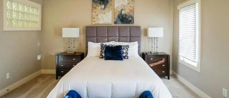 A bedroom with a large bed, two bedside tables, a ceiling fan, and artwork on the wall.