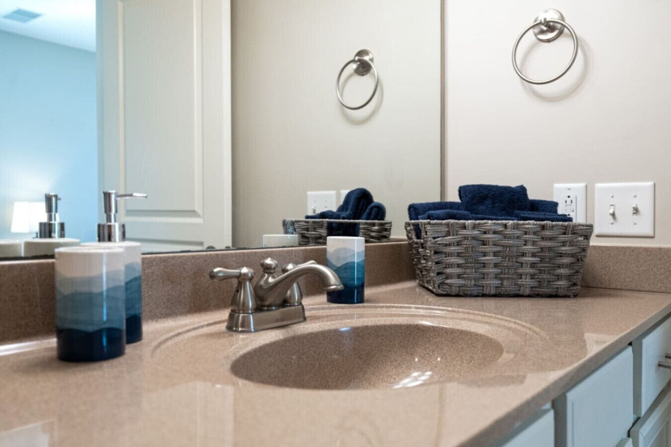 Een badkamer met een beige wastafel, een spiegel, een handdoekhouder, een rieten mand en een blauwe handdoek.