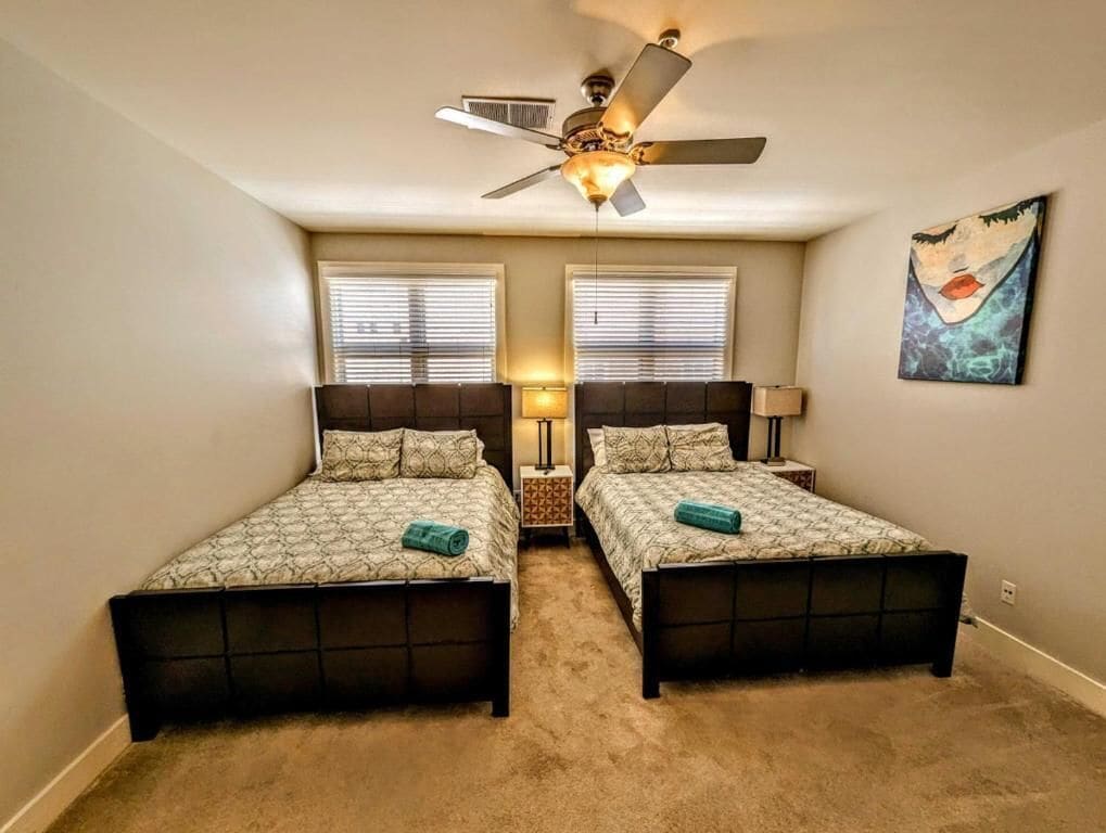 A bedroom with two beds, a ceiling fan, and a painting on the wall.