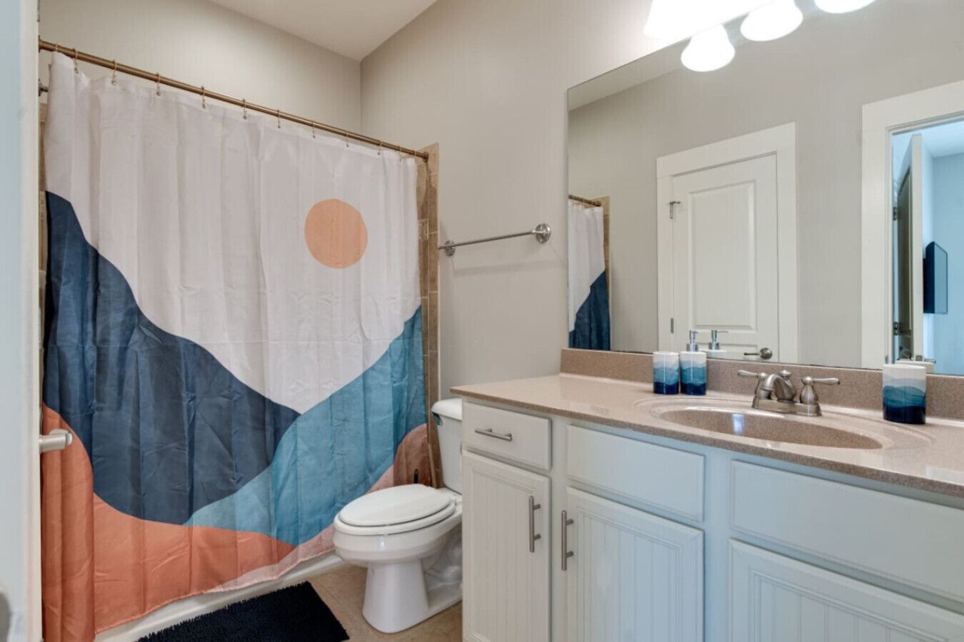 Un baño con cortina de ducha decorada con un diseño de montaña, inodoro, lavabo con espejo y armarios debajo.