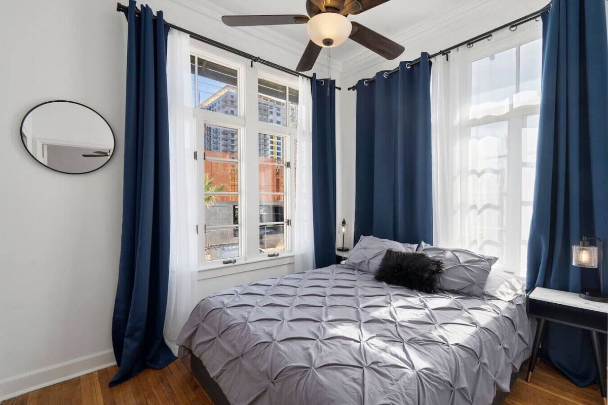 Quarto com cama, ventilador de teto e janela com cortinas.