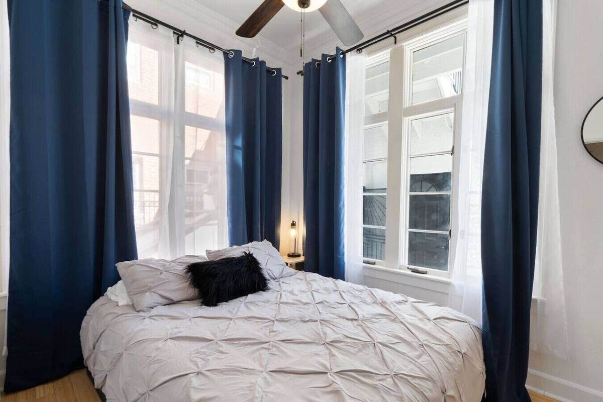 Quarto com cama, cortinas azuis e ventilador de teto.