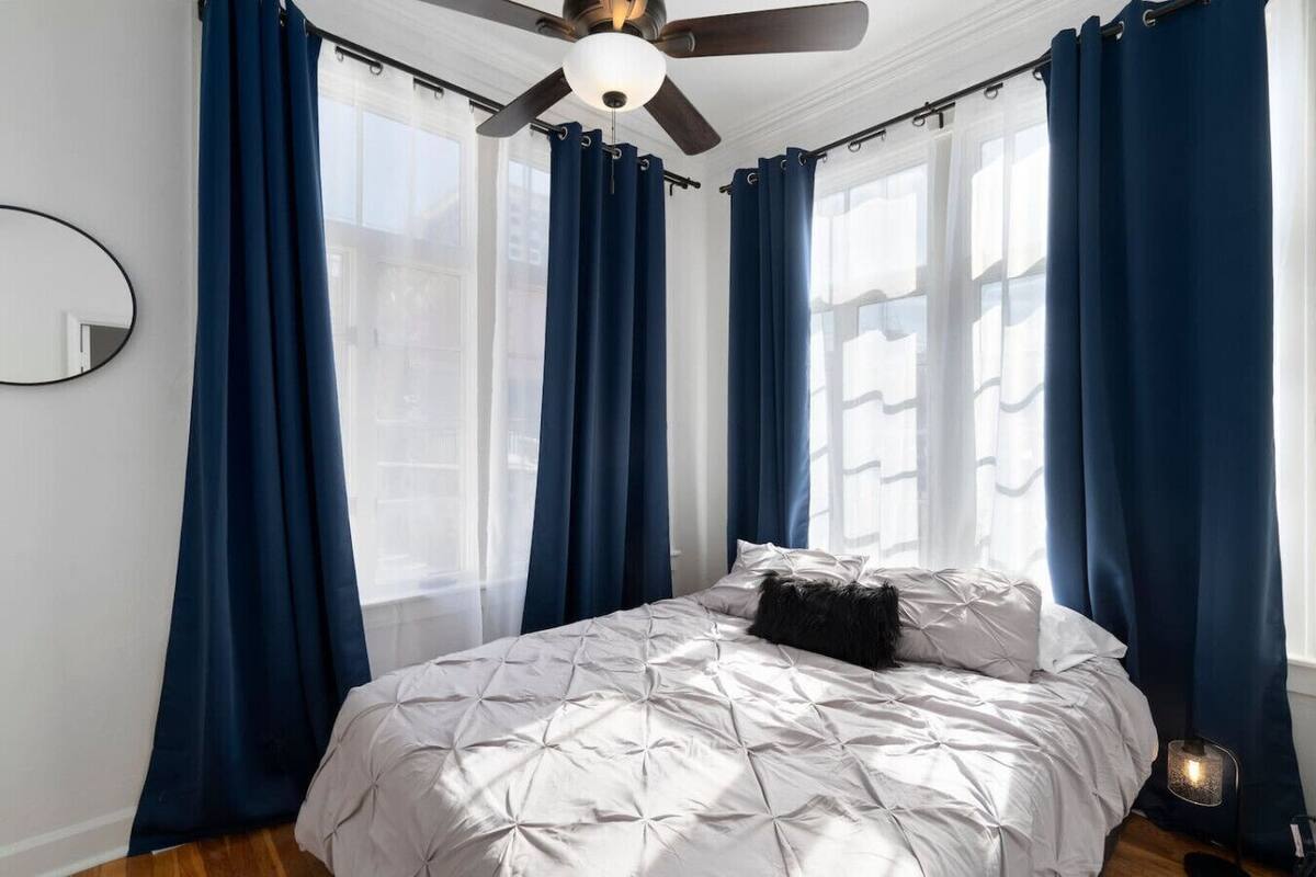 Quarto com cama, cortinas escuras, ventilador de teto e janela.