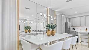 A modern kitchen with white cabinets, a large island with chairs, and a hanging light fixture.