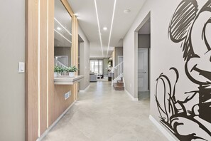 Step into a bright hallway adorned with sleek, modern lighting and a playful mural that adds character to the space. The warm wood accents and polished flooring invite you to explore the stylish living areas just beyond.