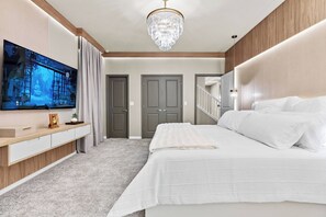 Enjoy a beautifully designed bedroom with plush carpeting and a chic chandelier that warmly lights the space. The spacious layout includes a sleek TV above a stylish wooden console, perfect for unwinding after your adventures.