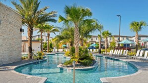 A swimming pool with a 3 ft depth marker, surrounded by palm trees and lounge chairs, with a brick wall and modern buildings in the background.