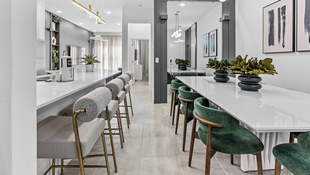 A modern kitchen with a long island, bar stools, and green chairs.