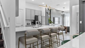 A modern kitchen with white cabinetry, a central island with bar stools, and a staircase leading to another level.
