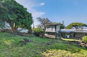 Una casa moderna con un porche cubierto, un muro de piedra y un árbol grande.